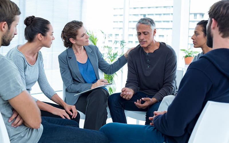 woman Counselor consoling middle age man in group therapy session