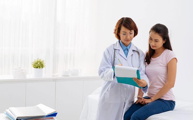 A Nurse with white lab coat reviewing chart with young woman sitting