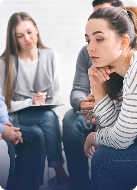 a women counselor with several patients in a group session with one young adult woman leaning her head on her hand seeming to be troubled.