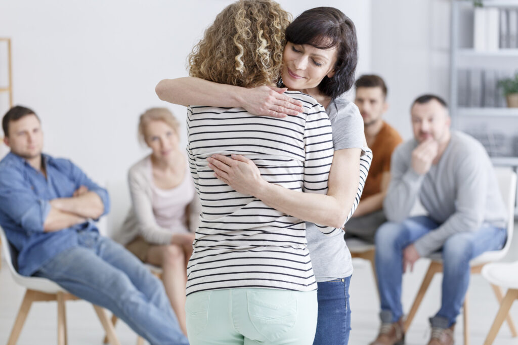 Group session of 6 adults with 2 women standing hugging
