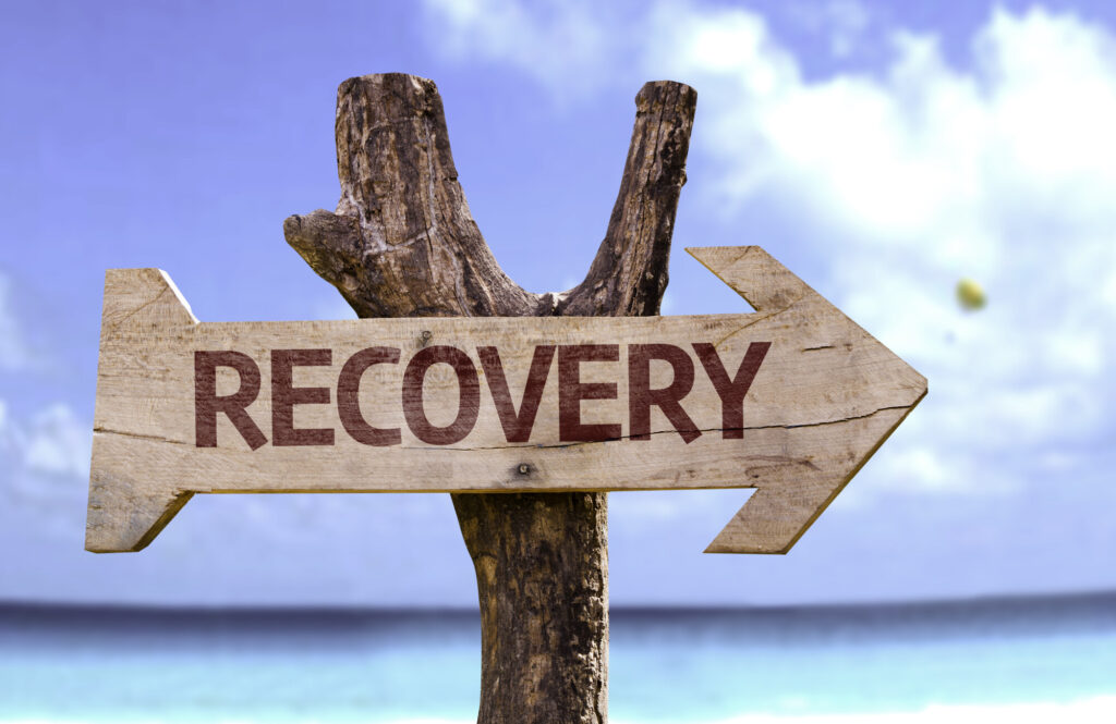The word RECOVERY on a wooden Arrow pointing with beautiful blue sky and ocean background