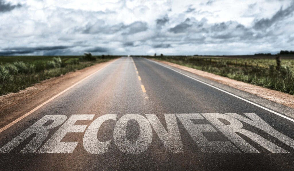 a road looking into the distance with the word RECOVERY written in white