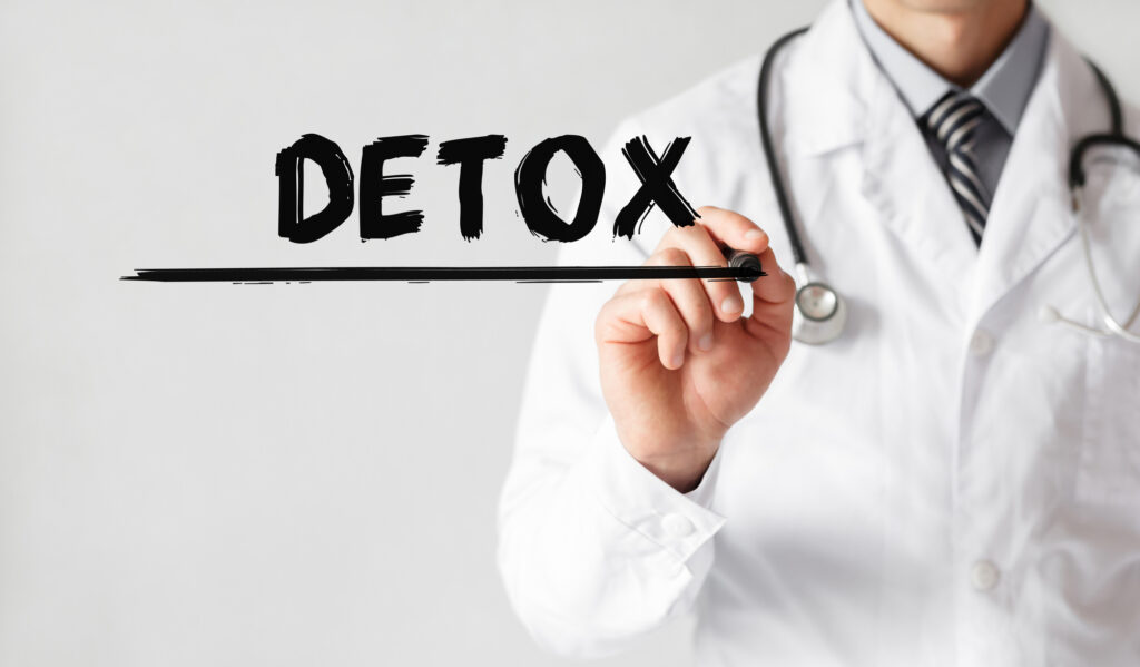 A Doctor in a white lab coat writing the word DETOX on a board